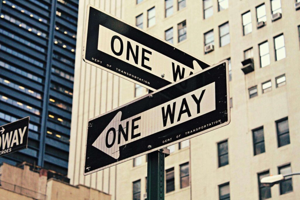 Two "ONE WAY" street signs pointing in different directions, representing the differences in the incorporation process and benefits between Singapore and Hong Kong