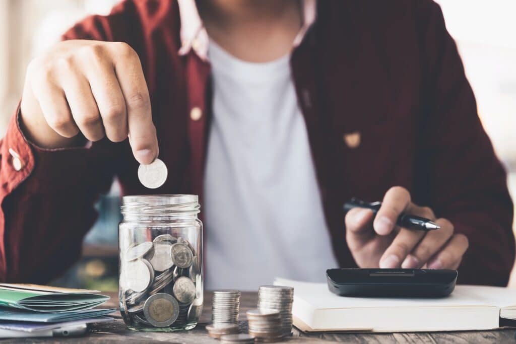 Business owner calculating the money earned from GST Refunds and putting coins in a jar.